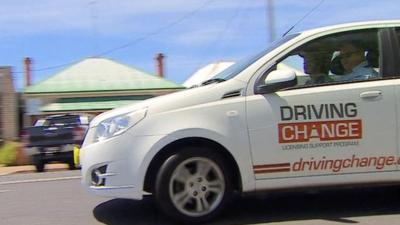 White car driving through town with Driving Change printed on the side