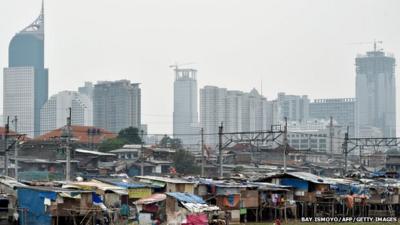 Shanty houses on a river bank in Jakarta, in shadow of skyscrapers