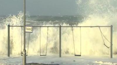 Waves crash over wall by playground swings