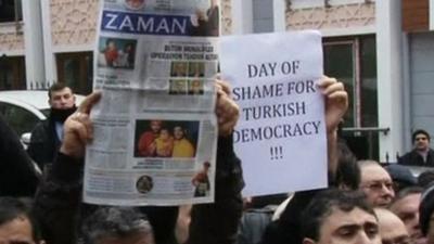 Protesters holding aloft the Zaman newspaper, the editor of which has been arrested, and a sign reading 'Day of shame for Turkish democracy!!!'