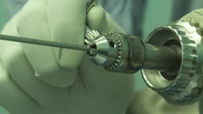 Close up of surgical drill being handled by someone wearing surgical gloves