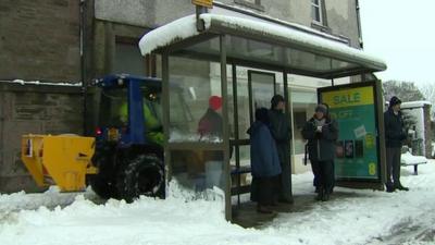 Gritter moving behind bus stop on snowy street