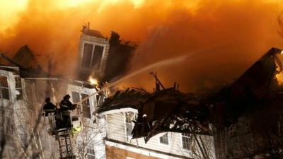 Firefighters stand on a ladder while hosing water onto an apartment complex, Wednesday, Jan 21, 2015, in Edgewater, NJ.