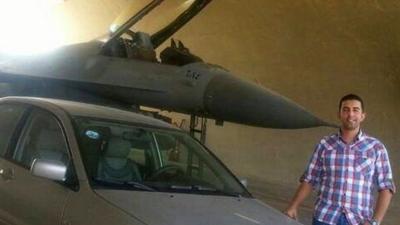 Moaz al-Kasasbeh next to a fighter jet and a car