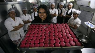 Pooja Dhingra holding a tray of macarons in front of some members of staff