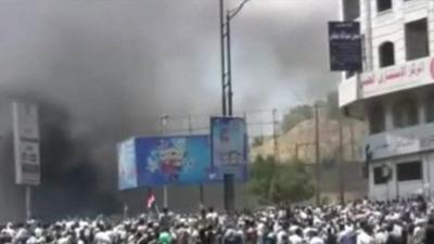 A crowd in Yemen with black smoke rising over the crowd