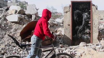 Boy on bike looks at door bearing Banksy artwork