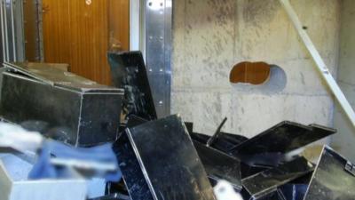 Safety deposit boxes in a pile with hole in wall behind them