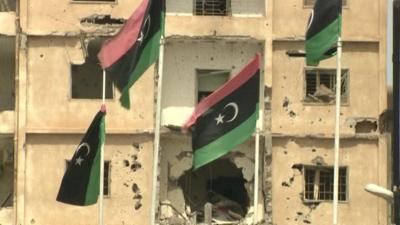 Badly damaged building and Libyan flags