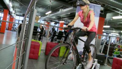 BBC Click's Lara Lewington rides a bicycle wearing a virtual reality headset