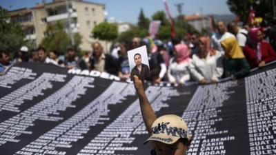 A youth holds a picture of one of the victims of the mining disaster that left over three hundred miners dead, as others hold a banner with their names, during a rally In Soma