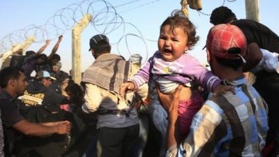 A Syrian refugee carries a baby after crossing over the broken border fence into Turkey from Syria in Akcakale, Sanliurfa province, southeastern Turkey