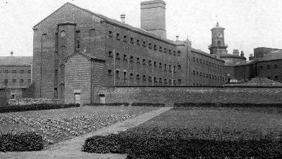A black and white photo of a large Victorian building, with a clock tower at the back.