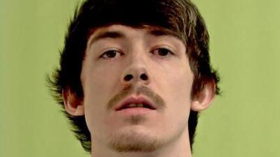 Police mugshot of Louis Thomas, who has short brown hair with a fringe and a thin moustache and beard on his chin.