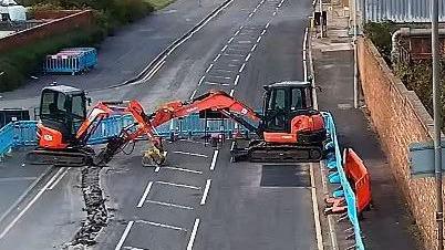 Two orange mini diggers working on repairing a road in St Helen.