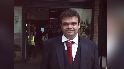 Jamie Sample, a man with dark hair in a suit and red tie.