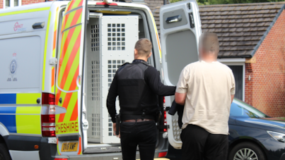 Rear view of a police officer arresting a man and leading him into the back of a police van 