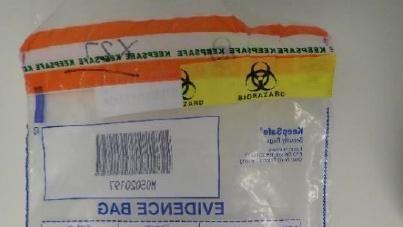 Part of a clear plastic bag. The bag has an orange and yellow band across the top and us make with blue lines and a barcode. The words "EVIDENCE BAG" written backwards are visible.