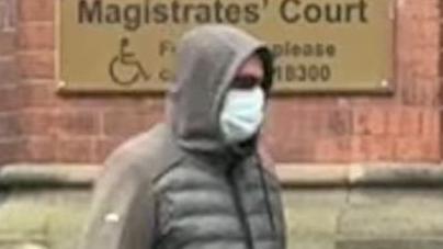 Man wearing a grey coat with a hood over his head walking outside a court wearing a face covering and dark glasses.