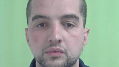 A police mugshot of Florian Roux, who has close-cropped dark hair and facial hair, against a green background.