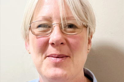 A woman with light coloured short hair and thin, metal framed glasses smiles into the camera.