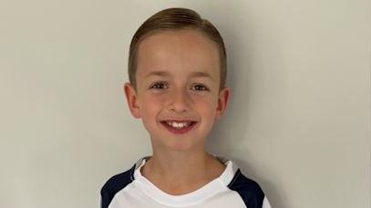 George Dennis smiling while wearing a white Tottenham Hotspur top.