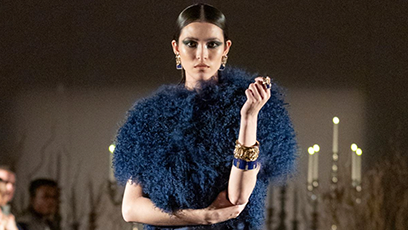 A model on a catwalk wearing a blue dress surrounded by an audience on either side of her