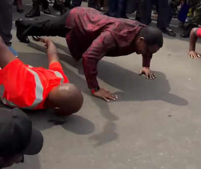 Lazarus Chakwera wearing a red shirt and black trousers doing push-ups in the street.