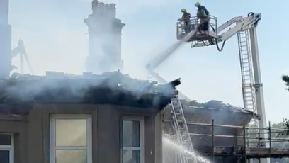 Firefighters on an aerial platform above a smouldering house.