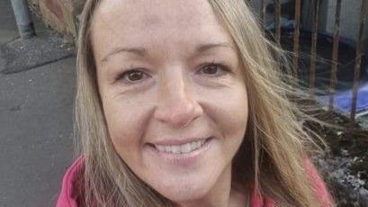 A woman with blonde hair and a pink jacket, smiling into the camera