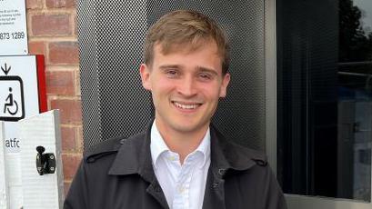 Labour MP Keir Mather wearing a black rain coat and white shirt