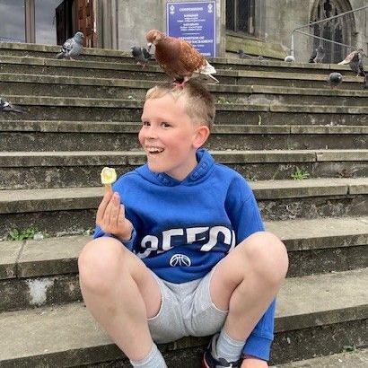 Young boy holding an ice cream, with a pigeon sitting on his head.