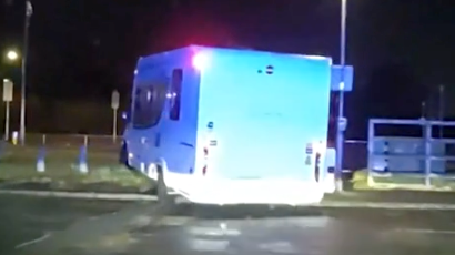 A still from a video showing the rear view of a white motorhome moving from a road to a grass verge.
