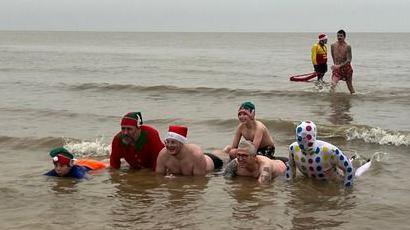 People in fancy dress taking part in a Christmas Day swim in Lowestoft. Six people are lying down in the water with two in the background standing up