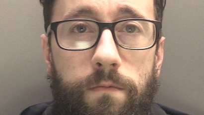 A police mugshot of Adrian Waring, 35, who has a brown beard , black hair and black framed glasses, and stares into the camera with a blank expression