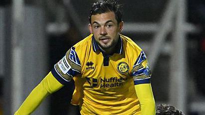 Jake Forster-Caskey in yellow Woking away shirt playing in a night match