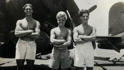 A black and white, old photo of three young men standing in front on aeroplanes. 