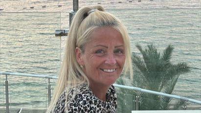 Anita Rose looks over her shoulder at the camera. In the background is the sea.