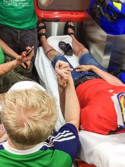 A Northern Ireland fan holds the hand of an injured Poland fan in an ambulance