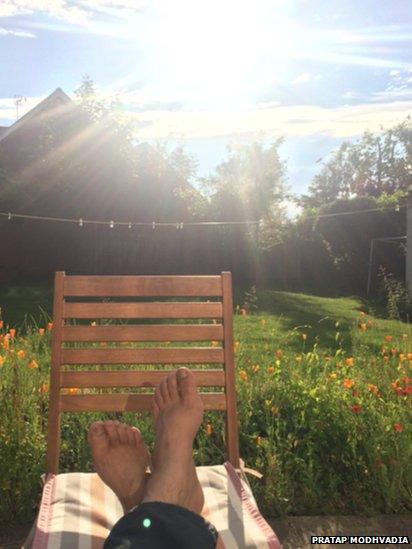 Someone's feet can be seen on a chair, as the sun shines down into a garden