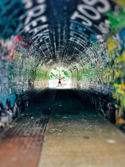 A-view-through-a-graffiti-covered-tunnel-with-someone-stood-at-the-far-end