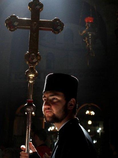 A Greek Orthodox altar boy holds up a ceremonial cross as a ray of light enters the church during the Orthodox Easter Sunday procession at the Church of the Holy Sepulchre in Jerusalem's Old City (April 15, 2012)