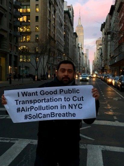 Oscar Soria holding a sign saying "I want good public transportation to cut #AirPollution in NYC #SoICanBreathe"