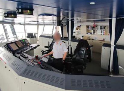 A man in a nautical uniform at the controls of a large ship