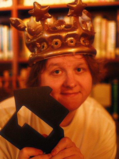 Lewis Capaldi holding a number one trophy with a blow up crown on his head