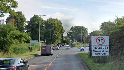 Cars drive in both directions on the main road. The photo shows a 30mph sign for Rugeley with trees on either side of the route.
