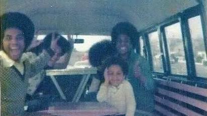 A group of people in the back of a vehicle, sitting on benches and looking at the camera. 