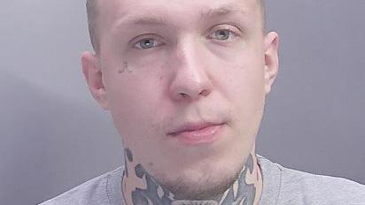 A close-up image of a man with short hair, with a large neck tattoo, and wearing a grey T-shirt.