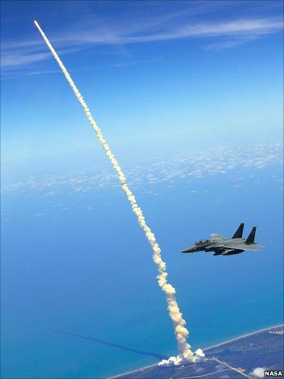 An F-15E Strike Eagle flies past as the Space Shuttle Atlantis (STS-132) launches from Kennedy Space Center, 2010