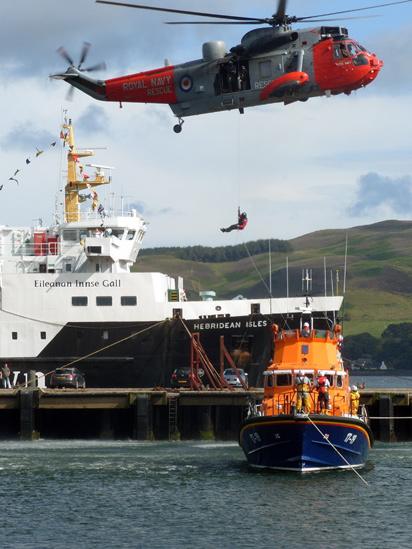 Man being winched from a lifeboat to a helicopter with a ferry in the background